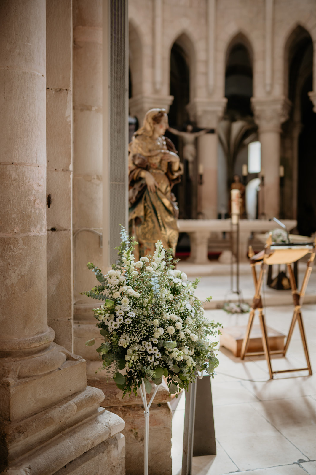 Interior em pedra de igreja histórica preparado para cerimónia de batizado, com arranjo floral branco